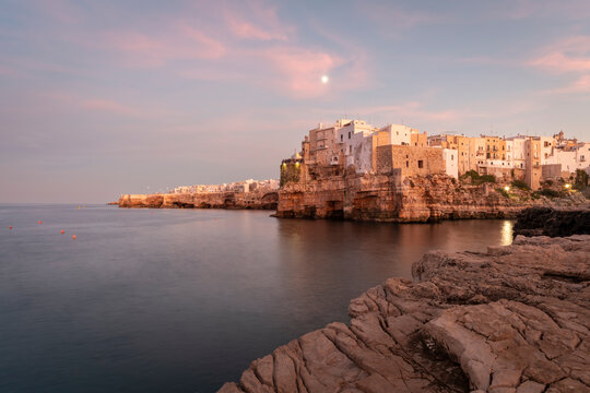 Polignano a Mare in Apulia, Italy at sunset with historic buildings on cliffs and calm sea