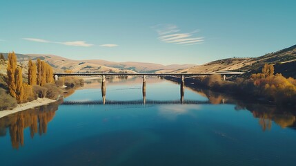 Fototapeta premium Overhead shot of a sleek bridge crossing a river, with reflections on the water and clear skies.