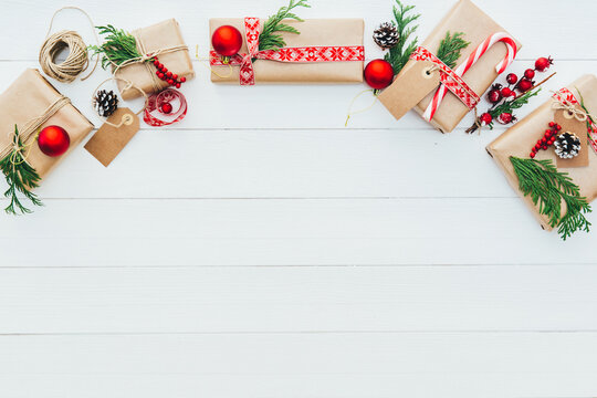 Overhead view of assorted wrapped Christmas gifts decorated with irons, fir branches, berries, pinecones and candy canes on a wooden table