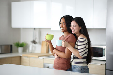 Happy interracial lesbian couple drinking affectionate in the kitchen
