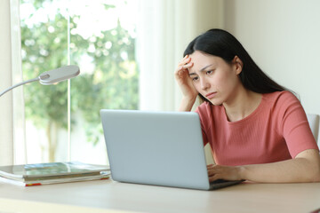 Worried asian woman checking bad news on laptop
