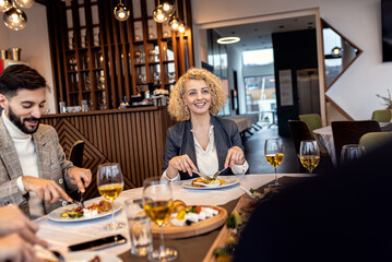 Portrait of businesswoman sitting with coworkers in restaurant, talking during business lunch.