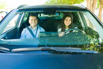 Portrait of happy teenager learning to drive with her instructor during driving test lesson