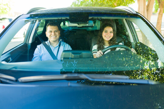 Portrait of happy teenager learning to drive with her instructor during driving test lesson