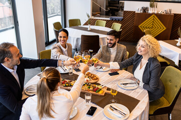 Smiling coworkers in restaurant toasting with wine during business lunch.