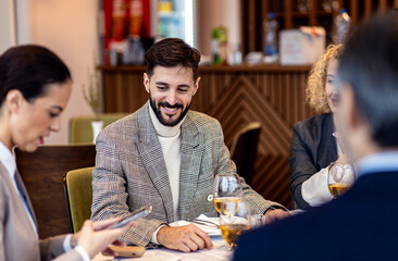 Portrait of businessman sitting with coworkers in restaurant, talking during business lunch.