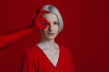 A woman in a red dress and a mysterious red hand makes an eyepiece gesture to her. To look at it...