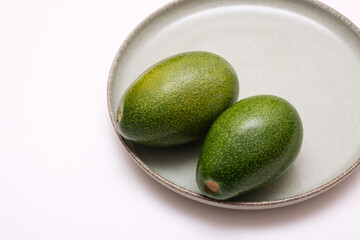 Two ripe avocados on a green plate. Fresh avocados on a ceramic plate, isolated on a white background.