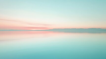 Fototapeta premium A soft, pastel-colored sunrise over a still lake with a distant mountain range.