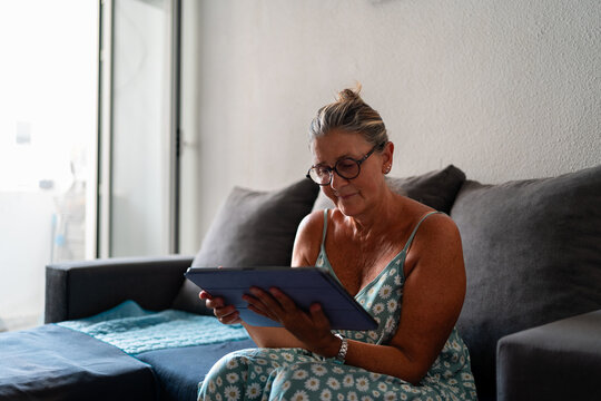 Focused mature woman using digital tablet while working remotely from home, enjoying comfortable and convenient online work environment