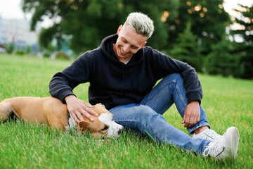 Obraz premium Dog lying on the grass, a Caucasian guy sits next to him and strokes the dog. friendship of a dog and a man. American bulldog.