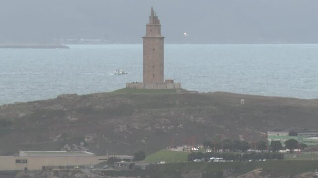 Pan of Tower of Hercules, lighthouse located in the Spanish city of A Coru&ntilde;a on a day with typical Galician weather with fog and rain with the sea hitting the rocks on which it is located