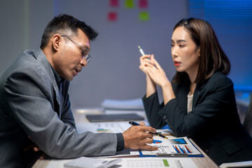 A man and a woman are sitting at a desk with papers and a pen