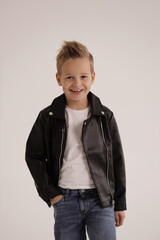 cute boy with blond hair wearing leather jacket and jeans posing in studio