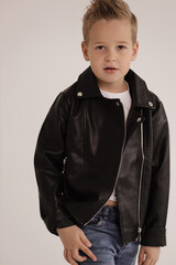 cute boy with blond hair wearing leather jacket and jeans posing in studio