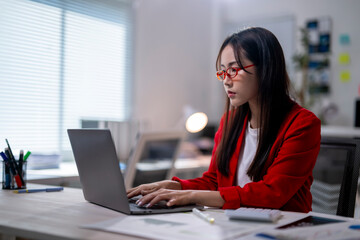 A woman in a red jacket is typing on a laptop computer