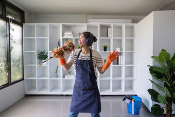 Happy young Asian woman dancing and singing with a feather duster while cleaning