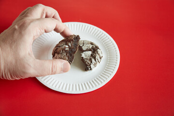 A hand taking a broken chocolate cookie with cracks from a white paper plate against a red background, close-up, homemade baking, chocolate cookies, treats on a plate.