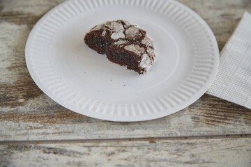 A paper plate with one half of a chocolate cookie with cracks on an old rustic wooden table and two paper napkins, close-up, half portion, diet, limiting dessert and pastry consumption.