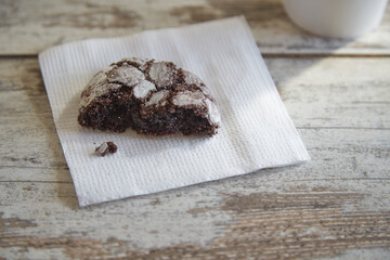 A paper napkin with one half of a chocolate cookie with cracks in a beam of sunlight on an old rustic wooden table, close-up, half portion, diet, limiting dessert and pastry consumption.