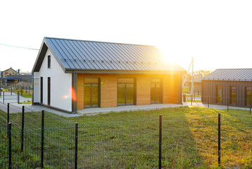 Obraz premium New modern home in gated community. Suburban house. Residential house in suburban neighborhood. Residential condominium home with fence, green lawn. Family Home on sunset. Villa in suburb. Dream Home.