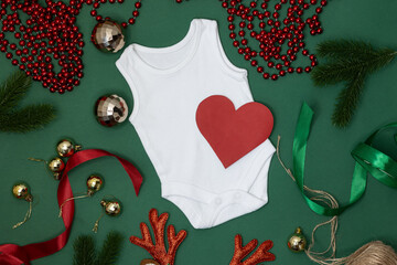 Newborn bodysuit on a green background with Christmas decor and a red heart. Report pregnancy at Christmas. Seasonal winter products for children and newborns. View from above. composition. Flat Lay