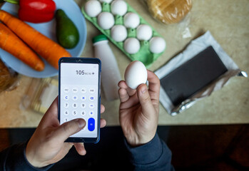 A man checks the calorie content of food products in a smartphone app. Calorie calculator for weight loss. On the table are products for consumption during a diet