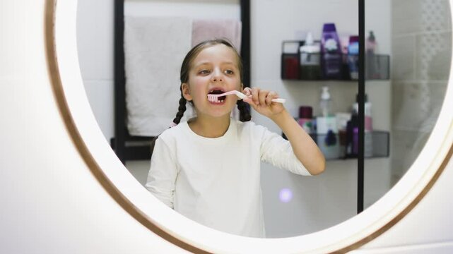 Caucasian girl with missing milk teeth brushing teeth in bathroom. She looks attentively in mirror, focusing on oral hygiene. Concept of childhood routines and dental care.