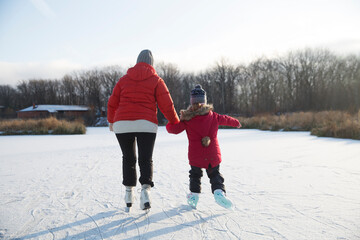 grandmother and little granddaughter skate on a frozen lake. grandmother teaches granddaughter to skate