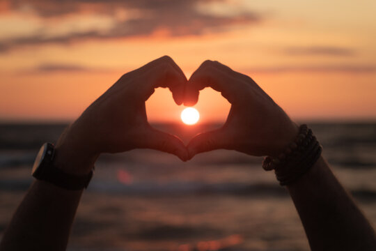 silhouette of hands and fingers forming heart in the sunset over ocean