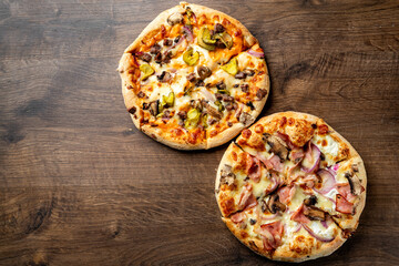Two delicious pizzas on a wooden surface: one topped with pepperoni, mushrooms, and peppers, and the other with ham, chicken, and olives. Perfect for sharing or a hearty meal.
