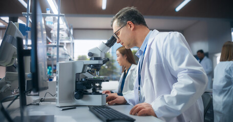 Excited Motivated Biotechnologist Studying Genetic Samples Under a Microscope and Researching Data on Computer in Order to Develop New Medical Products. Group of Scientists Working in a Laboratory