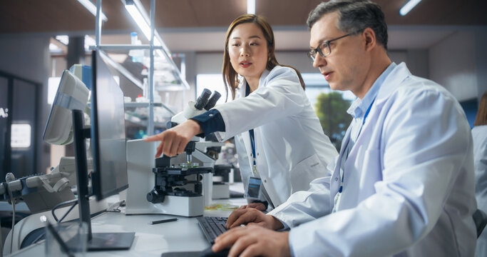 Asian Female Medical Supervisor Having a Conversation with a Caucasian Scientist About a Gene Editing Research Project, Crispr Technology and Experiments. Smart Diverse Team Working in a Laboratory