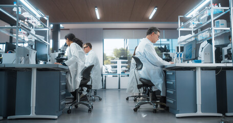 Fototapeta premium Team of Diverse Male and Female Medical Research Scientists Work Behind Desks on a New Generation Pharmaceutical Products in a Modern Laboratory. Colleagues Walking in the Background
