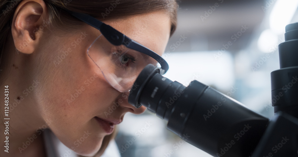 Poster close up portrait of a female microbiologist wearing safety glasses and looking through the microsco
