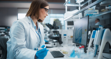 Caucasian Female Research Scientist Using Computer in a Modern Laboratory. Scientists are Conducting Research with the Help of Microscopes and Desktop Computers