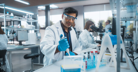 Indian Male Research Scientist Using Micropipette to Mix Liquids in a Test Tube in a Modern...