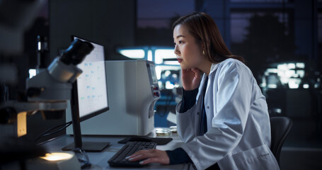Medical Research and Development Laboratory: Tired Japanese Female Scientist Working on a Computer with Advanced DNA Diagnostic Software. Modern Genetic Engineering Lab at Night © Gorodenkoff