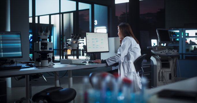 Asian Female Scientist Working on a Desktop Computer, Analyzing DNA Samples Alone in the Evening. Advanced Biotechnology Lab in a Medical Research and Development Center