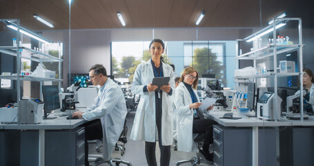 Group of Scientists in White Lab Coats Working in a Workplace, Sitting Behind Desks and Using...