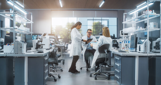 Modern Medical Laboratory: Scientists Working Together on a Research Project. Male and Two Young Women Talking About Vaccine Development Methods and Biotechnology Breakthroughs