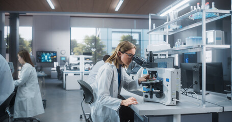 Naklejka premium Multiethnic Biotechnologists Studying Genetic Samples Under a Microscope and Researching Data on Computer in Order to Develop New Medical Products. Group of Scientists Working in a Laboratory