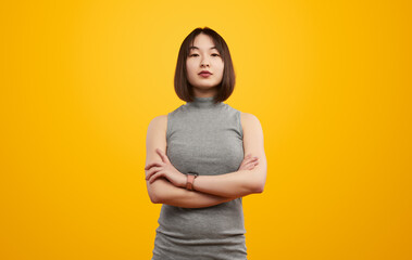 Portrait of confident young woman with arms crossed, standing against a bright yellow background,...