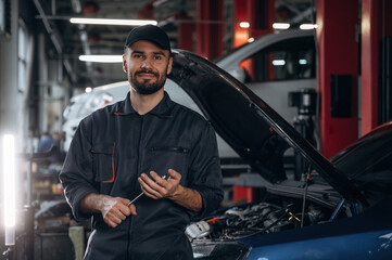 Front view, standing and holding tool. Mechanic working in a car service station