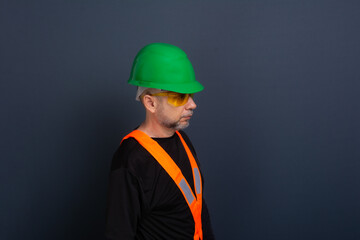 A civil worker wearing a green helmet, reflective vest and protective glasses. Posing for the photo. isolated on gray background.