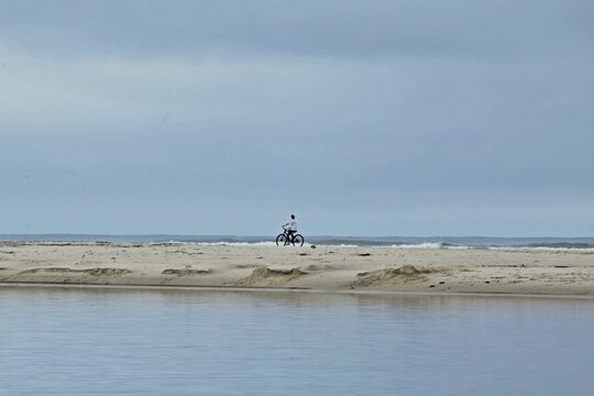 raia de Itaguare, Bertioga, Brazil with calm waters without waves, silhouette of a young woman riding a bicycle on the beach sand. Morning, sunless weather, deserted beach
