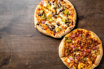 Two delicious pizzas on a wooden surface: one topped with pepperoni, mushrooms, and peppers, and the other with ham, chicken, and olives. Perfect for sharing or a hearty meal.