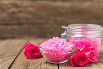 Sea salt for bath with aroma and rose flowers on textured wooden background. Pink sea salt. Spa treatments. Natural salt with herbs and essential oils. skincare concept. Meso for text. Copy space