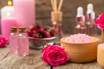 Sea salt for bath with aroma and rose flowers on textured wooden background. Pink sea salt. Spa treatments. Natural salt with herbs and essential oils. skincare concept. Meso for text. Copy space