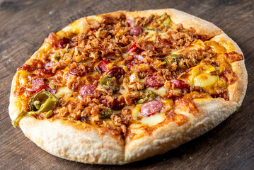 Close-up of a delicious pizza topped with crispy bacon, pepperoni, green peppers, and melted cheese, served on a rustic wooden surface. Perfect for food lovers and culinary themes.